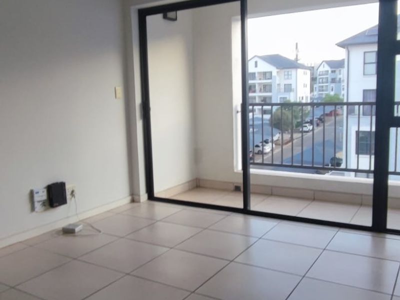 An empty living room featuring neutral tiled flooring and a large sliding glass door providing access to a private balcony.