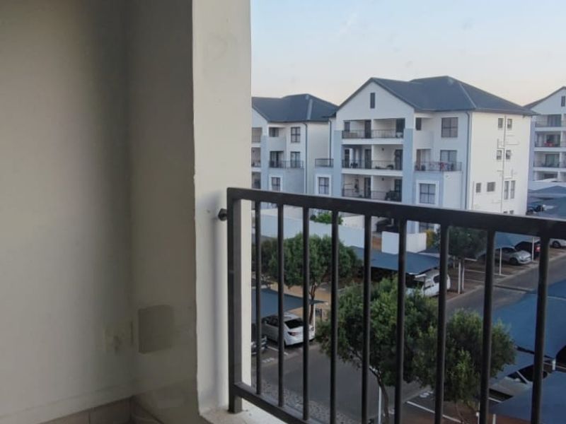 A covered balcony featuring tiled flooring and a metal balustrade, offering an elevated view of the surrounding apartment complex and parking area.