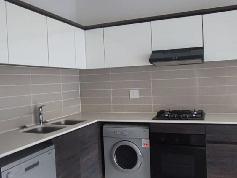 Modern kitchen featuring white and dark wood cabinetry, tiled backsplash, gas hob, built-in oven, and integrated space for laundry appliances.