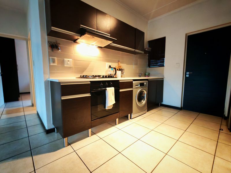 Modern kitchen featuring dark wood cabinetry, built-in oven, gas hob, extractor fan, and tiled flooring with integrated laundry plumbing.