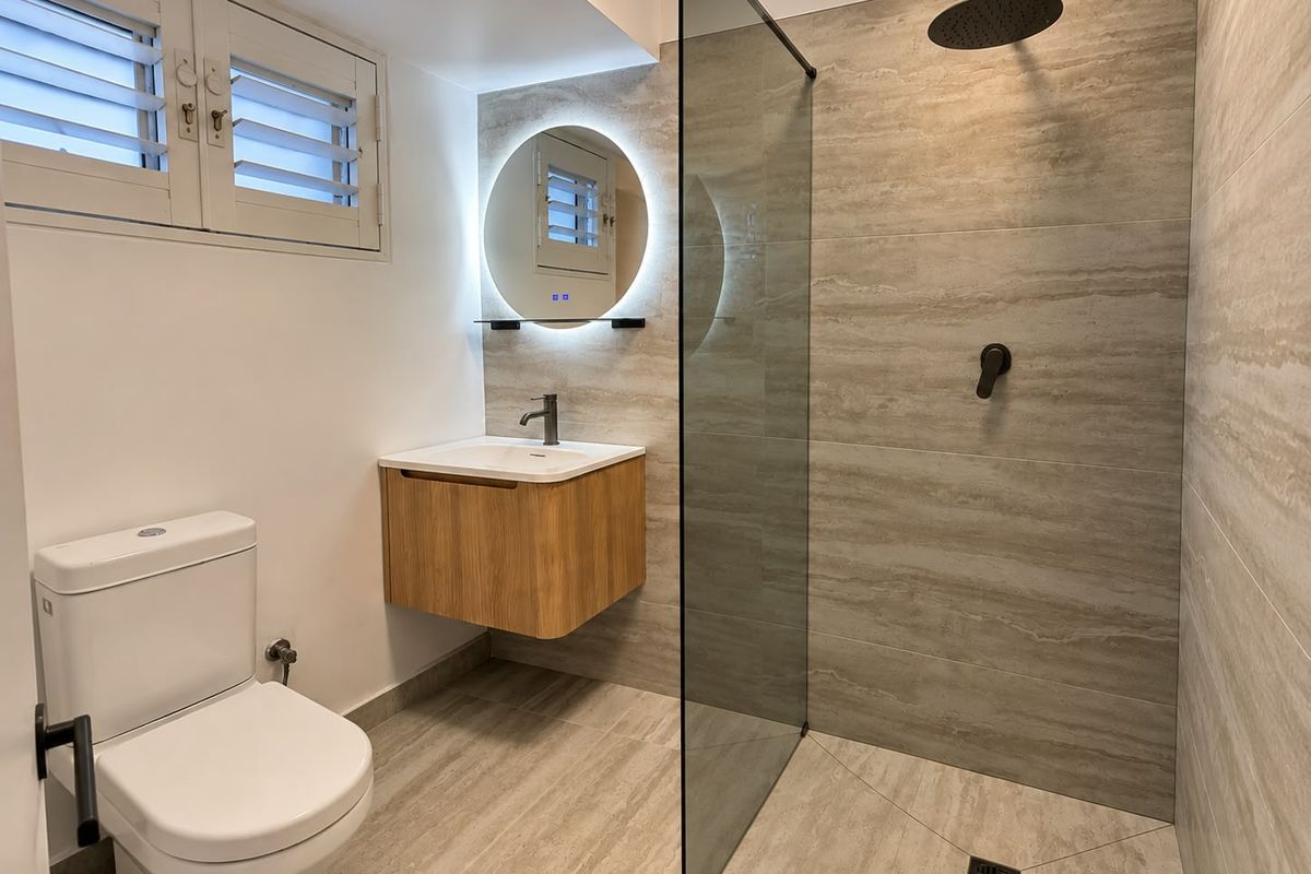 Modern renovated bathroom featuring a walk-in shower with rain head, floating vanity, backlit mirror, and neutral stone-look tiling throughout.