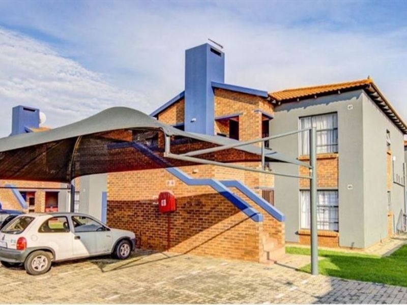 Exterior view of a brick townhouse complex featuring a paved driveway, shade cloth carport, and external staircase access to upper levels.