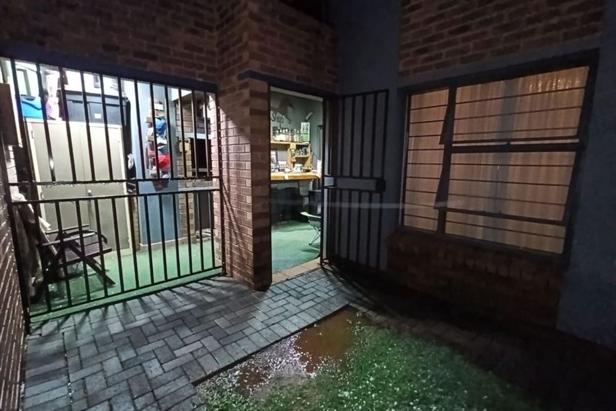 Rear exterior view of a townhouse featuring brick walls, security gates, and a paved patio area with visible drainage issues.