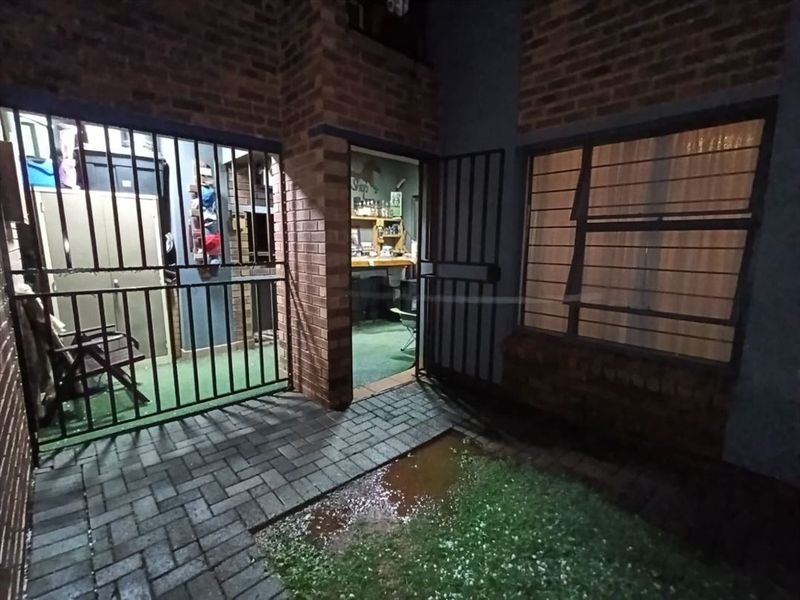 Rear exterior view of a townhouse featuring brick walls, security gates, and a paved patio area with visible drainage issues.
