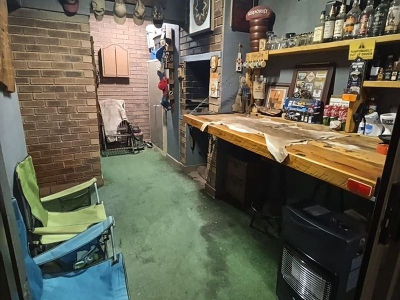 A rustic indoor bar area featuring a built-in brick fireplace, wooden bar counter, and fixed shelving, offering potential for a cozy entertainment space.