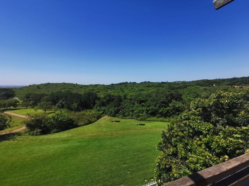 A scenic elevated view overlooking lush green hills and landscaped grounds, captured from a balcony.