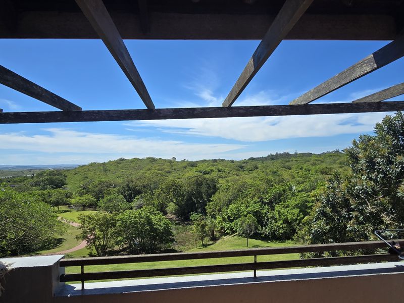 A balcony featuring a wooden pergola structure and metal railing, offering expansive views over the surrounding green landscape.