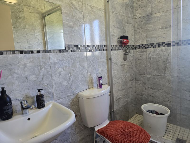 A modern bathroom featuring grey marble-effect wall tiles, a glass shower enclosure, a wall-mounted mirror, and a clean ceramic basin and toilet suite.