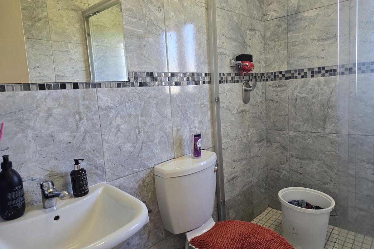 A modern bathroom featuring grey marble-effect wall tiles, a glass shower enclosure, a wall-mounted mirror, and a clean ceramic basin and toilet suite.