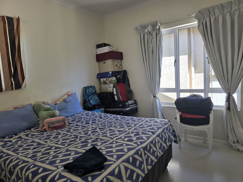 A standard bedroom featuring neutral walls, cove cornicing, and an aluminium-framed window with curtains.