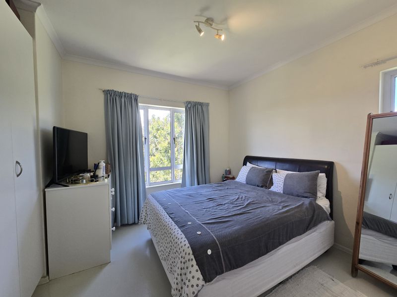 A well-lit bedroom featuring a built-in wardrobe, coved ceilings, and an aluminium-framed window providing natural light.