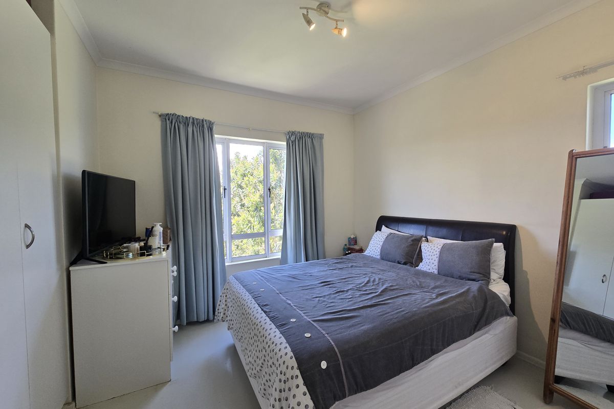 A well-lit bedroom featuring a built-in wardrobe, coved ceilings, and an aluminium-framed window providing natural light.