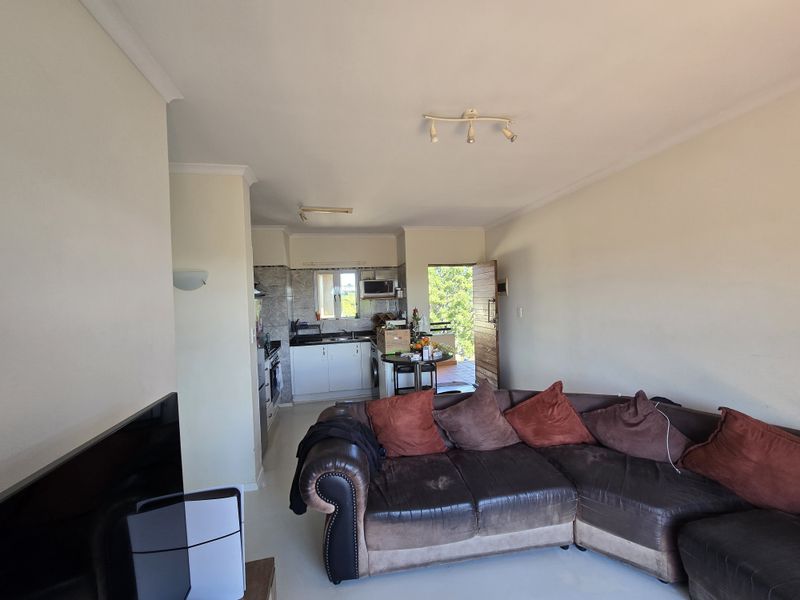 Open-plan living area featuring a functional kitchen with built-in cabinetry, oven, and hob, seamlessly flowing into the lounge space with direct access to a balcony.