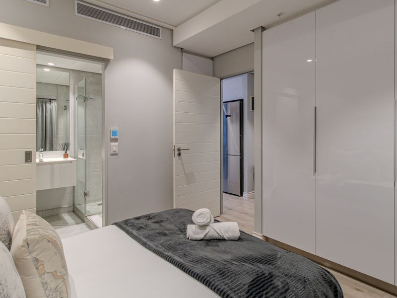 Modern bedroom featuring high-gloss built-in wardrobes, recessed lighting, and direct access to a sleek en-suite bathroom with a glass-enclosed shower.