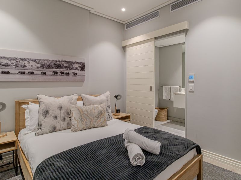 A modern, well-maintained bedroom featuring neutral tones, recessed lighting, ducted air conditioning, and a convenient sliding door leading to an en-suite bathroom.