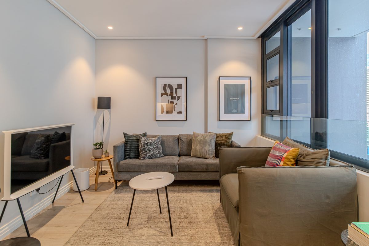 A modern, well-lit living room featuring large windows with a glass balustrade, recessed lighting, and light-toned laminate flooring.