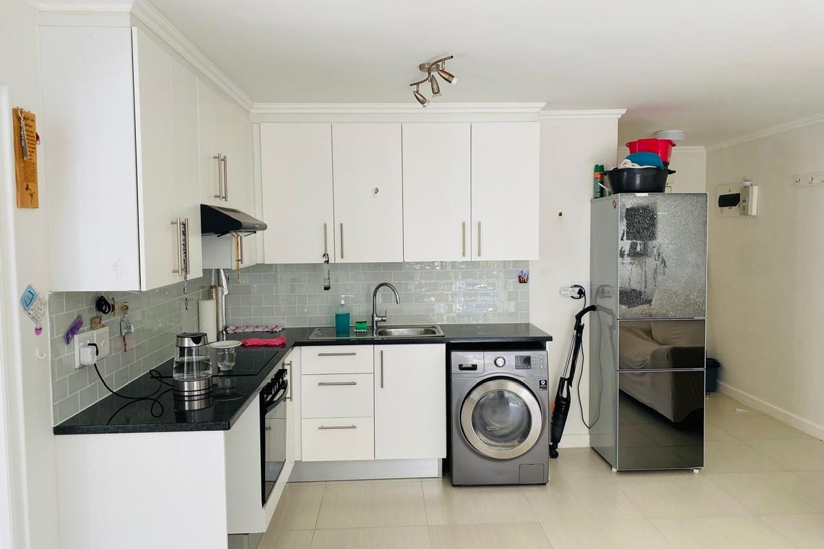 A functional kitchen featuring white cabinetry, dark granite countertops, subway tile backsplash, and integrated appliances including an oven and washing machine.