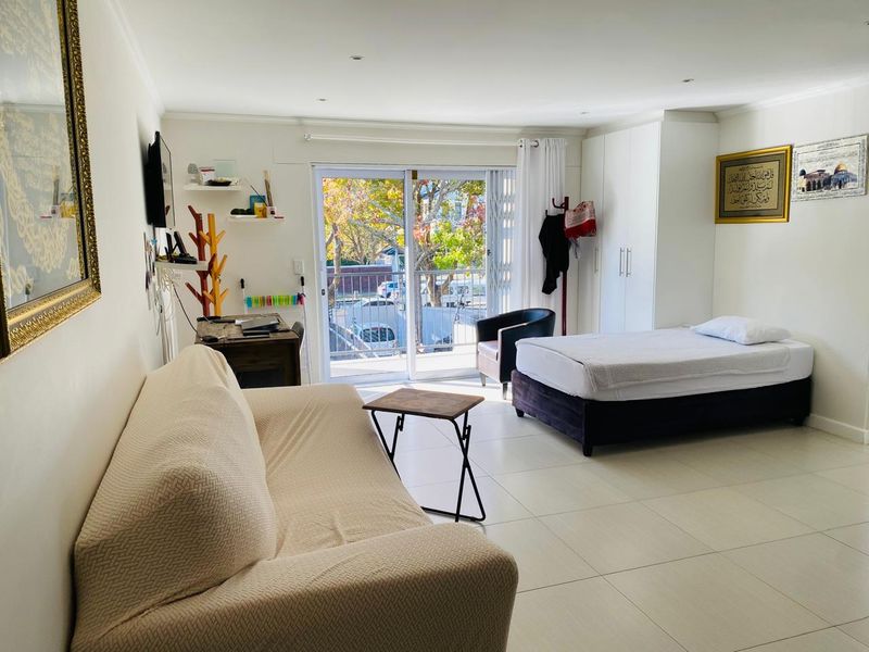 An open-plan living and bedroom area featuring tiled flooring, built-in wardrobes, and a sliding glass door leading to a balcony.