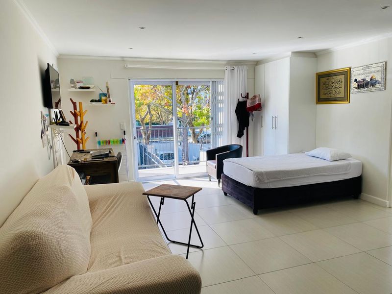 An open-plan studio apartment featuring tiled flooring, built-in wardrobe storage, and a sliding glass door leading to a balcony.