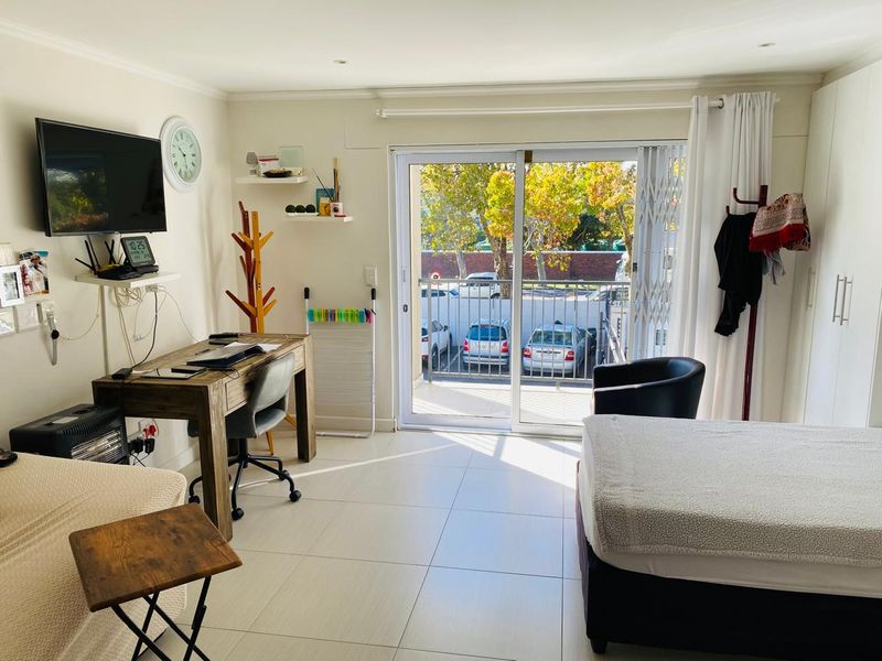 A bright bedroom featuring tiled flooring, built-in wardrobes, and a sliding glass door that opens onto a balcony with exterior views.