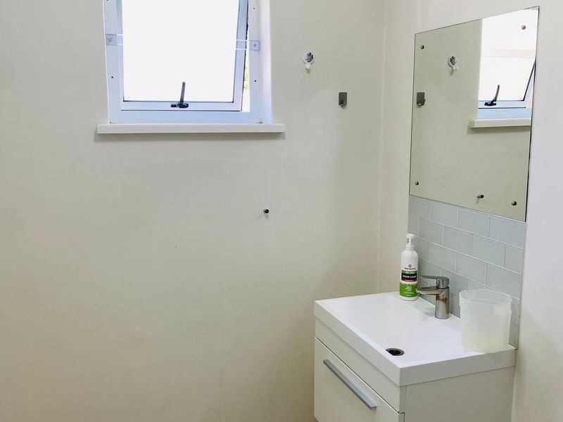 A compact bathroom featuring a modern wall-mounted vanity, tiled splashback, and a functional casement window, providing a clean and minimalist space.