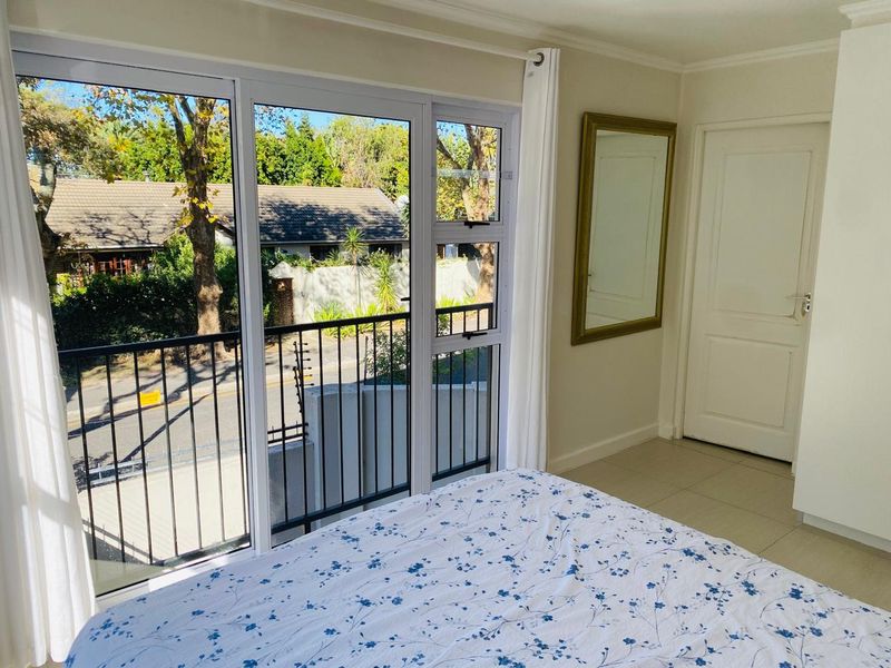 A bright bedroom featuring tiled flooring, a built-in cupboard, and a sliding glass door that opens onto a balcony with street views.