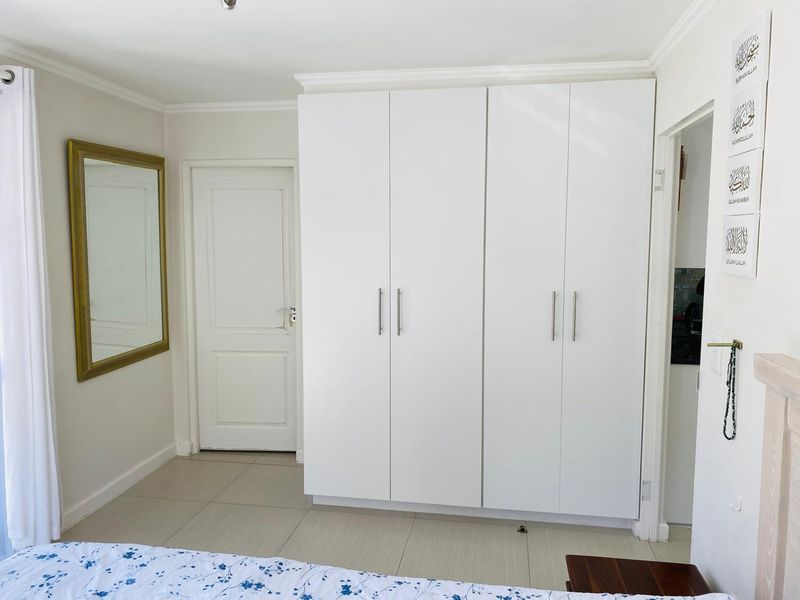 A well-maintained bedroom featuring neutral tiled flooring and a large, modern white built-in wardrobe with sleek handles.