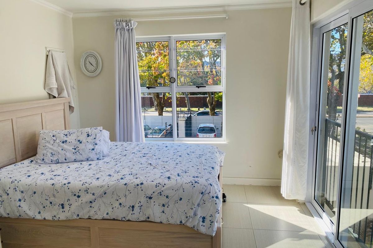 A bright bedroom featuring tiled flooring, large aluminium-framed windows, and a sliding glass door providing access to an outdoor area.