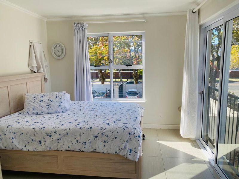 A bright bedroom featuring tiled flooring, large aluminium-framed windows, and a sliding glass door providing access to an outdoor area.