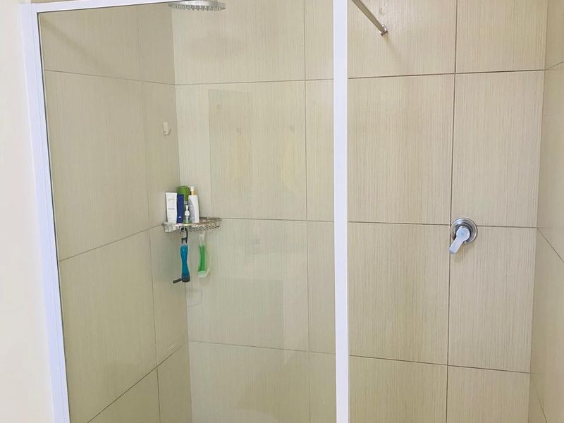 A modern bathroom featuring a walk-in shower with a glass screen, neutral wall tiling, and a tiled floor.