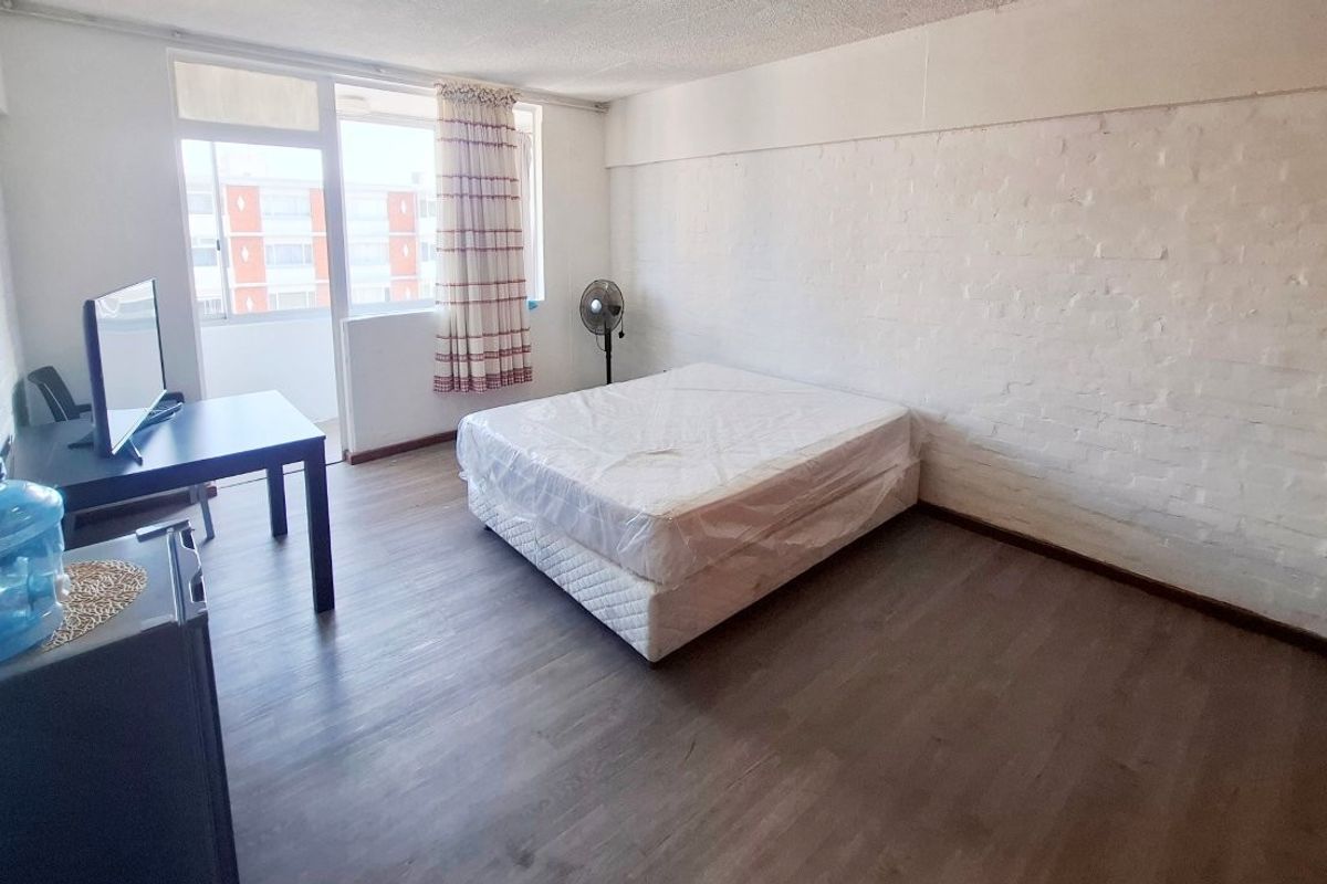 A spacious bedroom featuring laminate flooring, painted brick walls, and a sliding glass door leading to an attached balcony area.