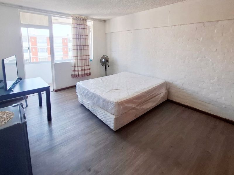 A spacious bedroom featuring laminate flooring, painted brick walls, and a sliding glass door leading to an attached balcony area.