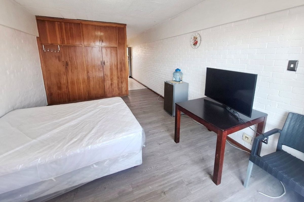 A bedroom featuring built-in wooden wardrobes, painted brick walls, and laminate flooring, offering a functional space with potential for modern updates.