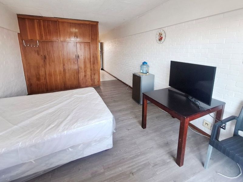 A bedroom featuring built-in wooden wardrobes, painted brick walls, and laminate flooring, offering a functional space with potential for modern updates.