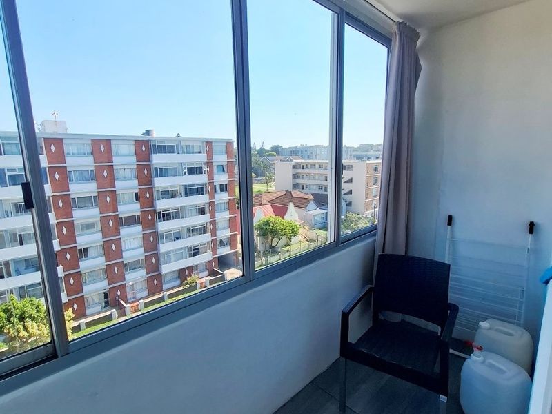 Enclosed balcony featuring large glass windows with urban views and tiled flooring, offering a versatile space for relaxation or storage.
