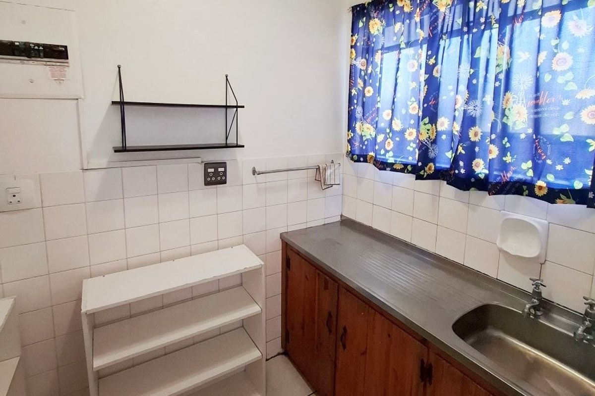 A functional kitchen area featuring wooden cabinetry, a stainless steel sink, tiled splashbacks, and tiled flooring.