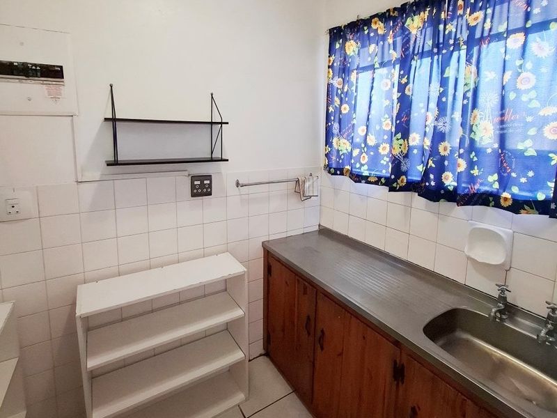 A functional kitchen area featuring wooden cabinetry, a stainless steel sink, tiled splashbacks, and tiled flooring.