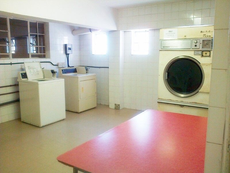 A functional communal laundry area featuring tiled walls, durable flooring, and multiple laundry appliance connections in a dated but practical layout.