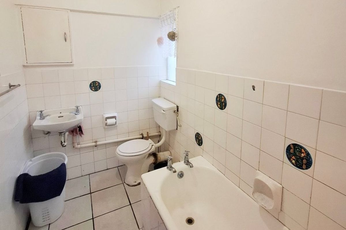 A functional bathroom featuring a bathtub, wall-mounted basin, and toilet with classic white tiling and exposed plumbing elements.
