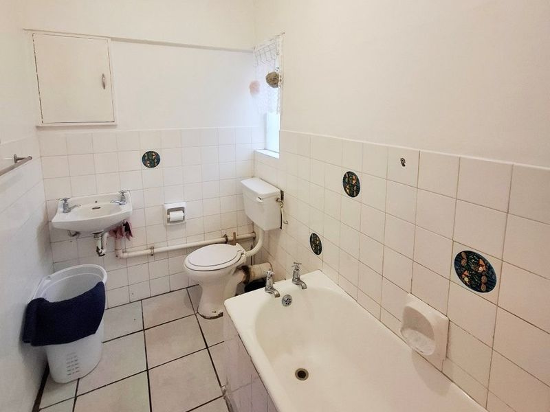 A functional bathroom featuring a bathtub, wall-mounted basin, and toilet with classic white tiling and exposed plumbing elements.