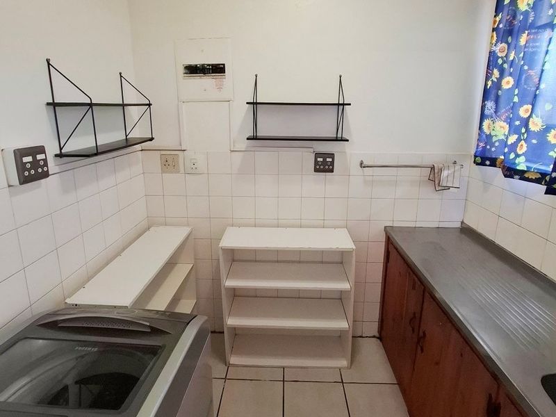 Functional laundry area featuring tiled splashbacks, built-in cabinetry with a metal sink, and tiled flooring, providing a practical space for utility tasks.
