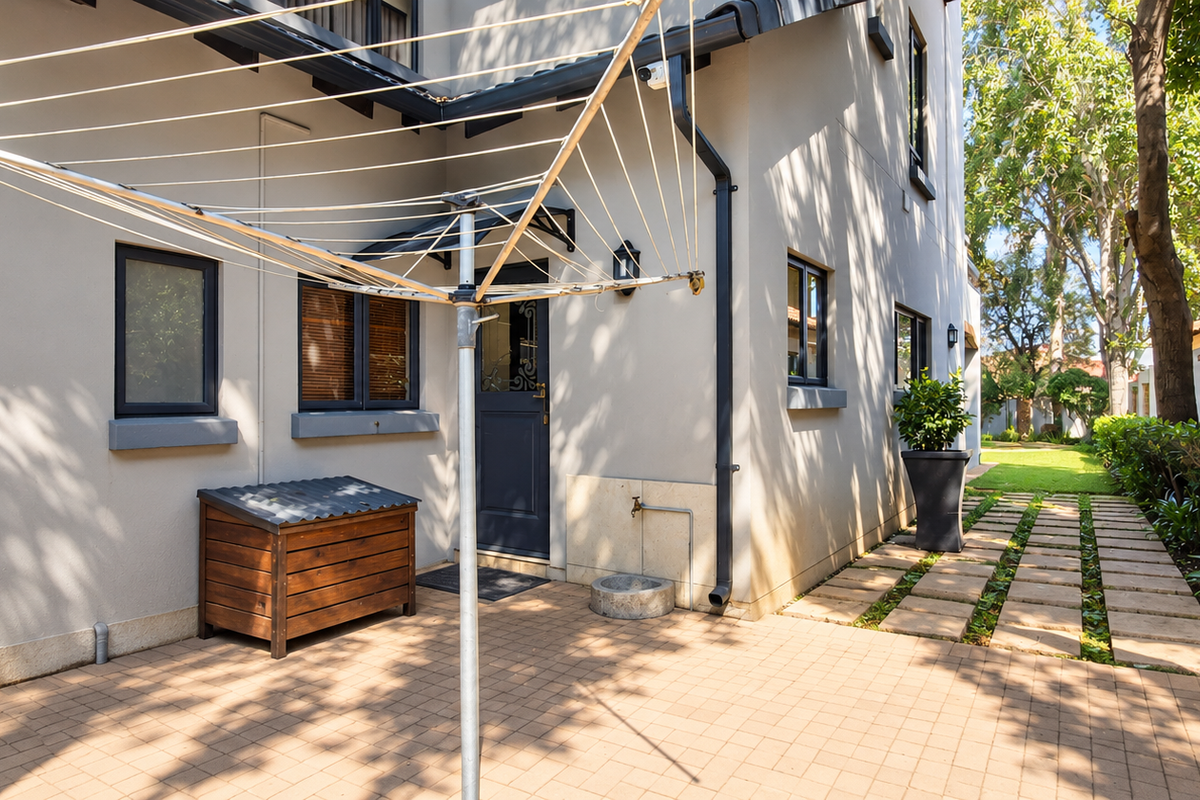 A well-maintained rear exterior area featuring a paved patio, a walkway leading through the garden, and functional outdoor infrastructure.