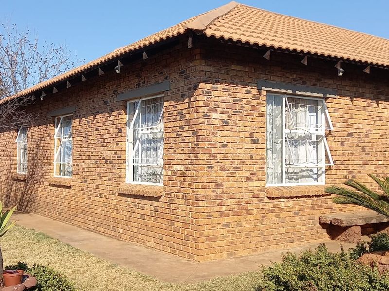 A view of the rear exterior of a face brick house featuring a tiled roof and multiple casement windows set within a landscaped garden.
