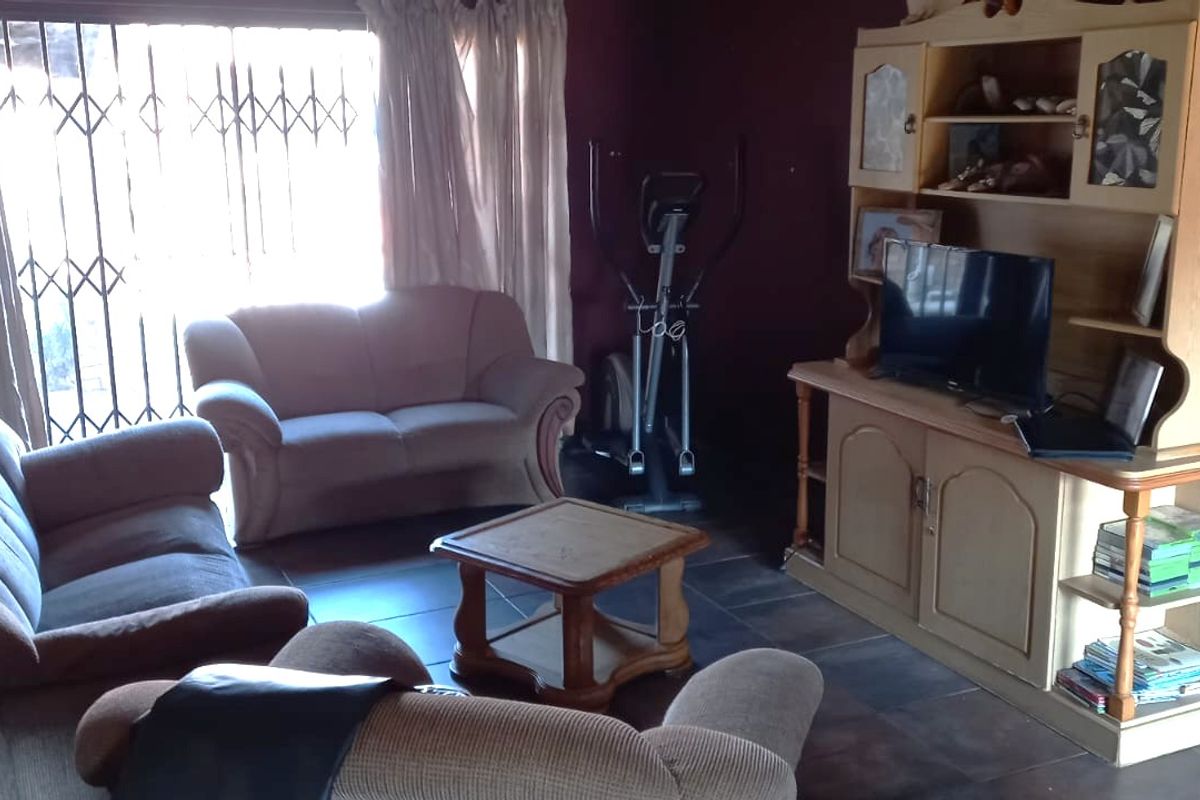 A living room featuring dark tiled flooring and a sliding door with a security gate, providing access to the exterior.