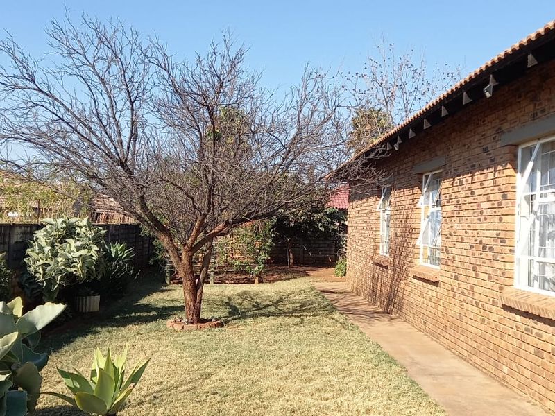 A view of the rear exterior of the house featuring face brick walls, tiled roofing, security bars on windows, and a garden area.