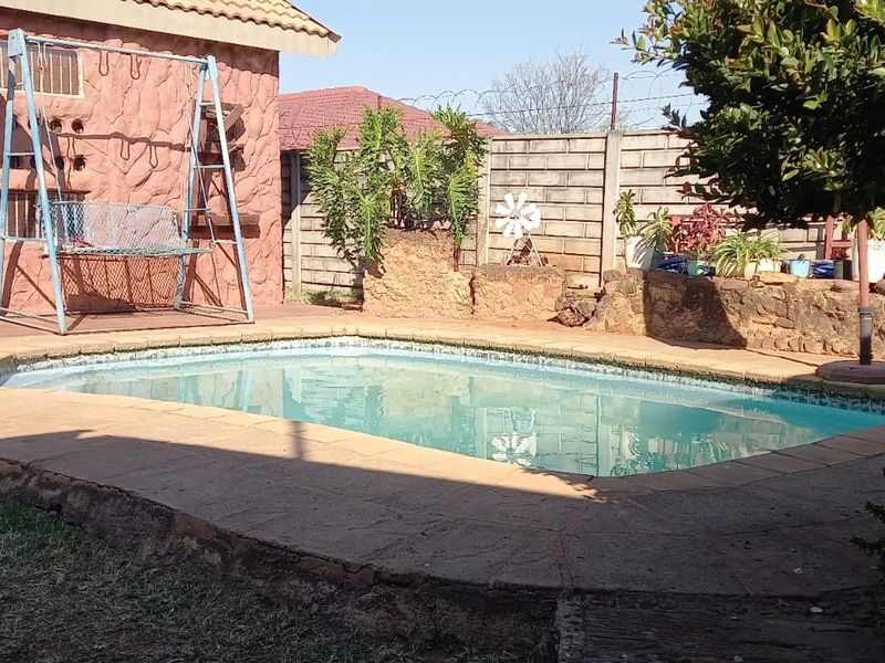 Outdoor pool area featuring a swimming pool with concrete coping, stone retaining walls, and a concrete block boundary wall with security fencing.