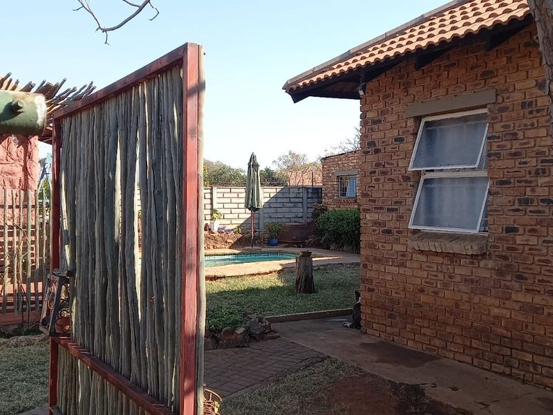 Rear exterior view of a face brick house featuring a paved walkway, small garden area, and a swimming pool in the background.
