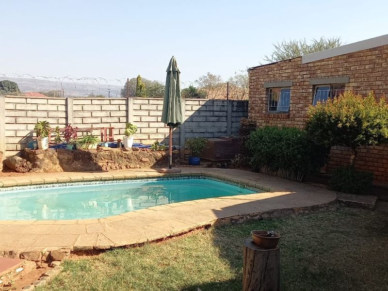 Outdoor pool area featuring a swimming pool with paved surround, enclosed by a brick boundary wall and adjacent to an exposed brick building.