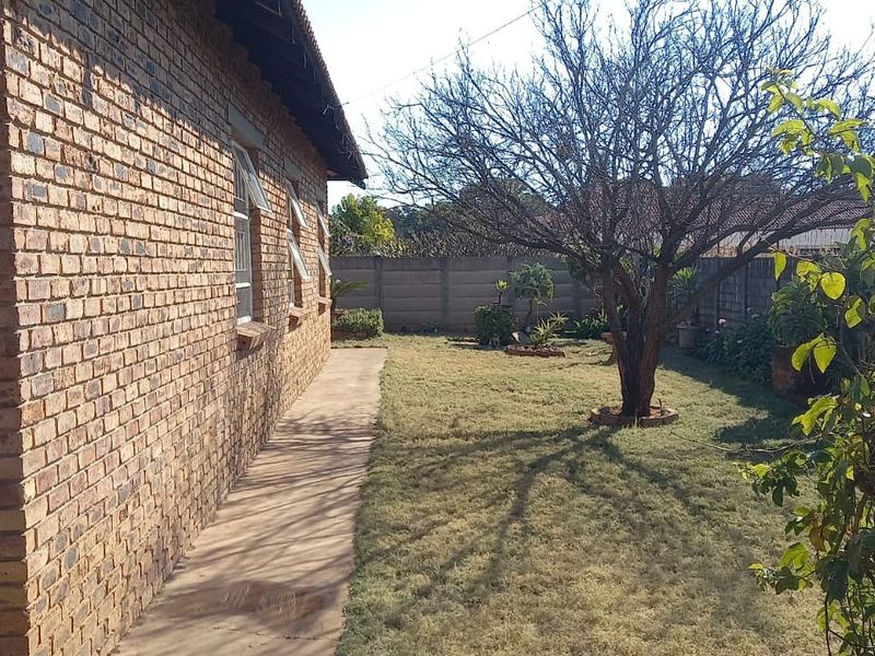 A view of the rear garden featuring a face brick exterior wall, a concrete pathway, and a precast concrete boundary wall.