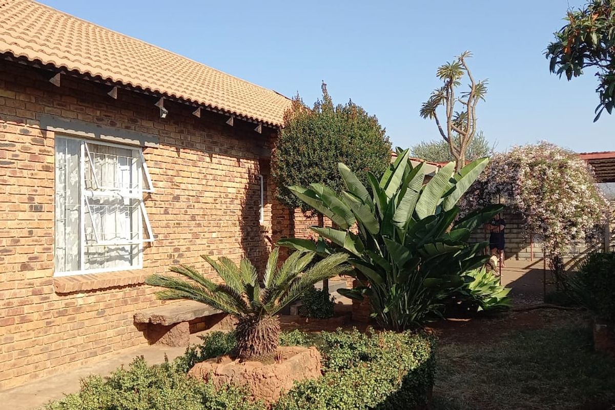 A rear view of the house featuring a face brick exterior, tiled roof, and established garden with a stone bench.